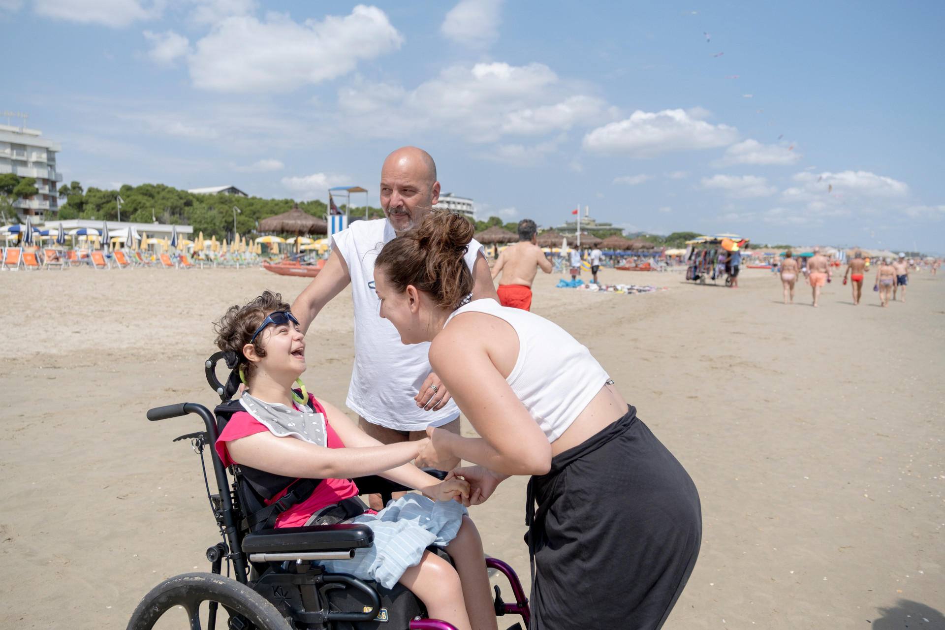 Una ragazza in carrozzina sorride mentre due educatori la fanno ballare sulla spiaggia durante il soggiorno estivo: un momento di gioia, movimento e inclusione.