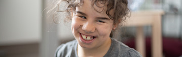 Giulia, bambina di 10 anni seguita al Centro di Osimo, sorride seduta per terra in un'aula del Centro Nazionale della Lega del FIlo d'Oro
