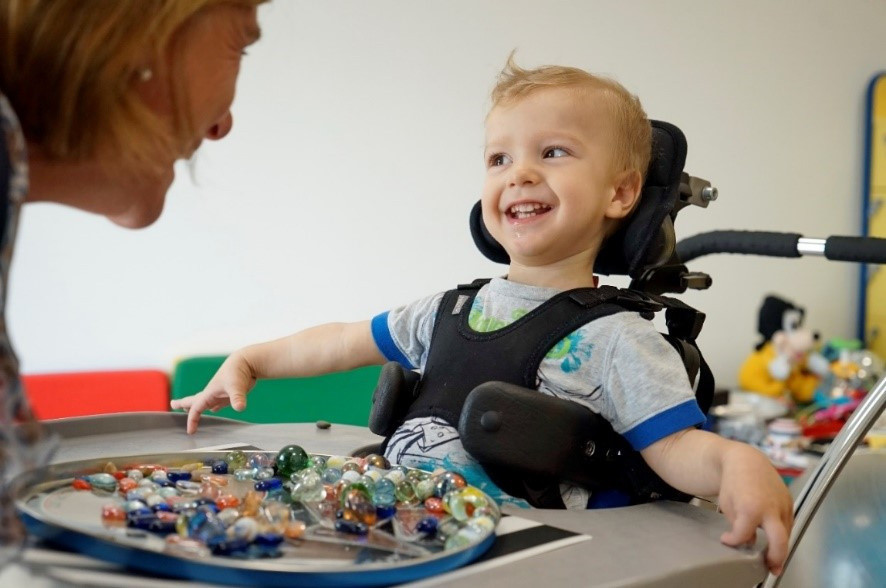 Riccardo, un piccolo utente della Lega del Filo d'Oro sorride mentre lavora con la sua educatrice. Immagine utilizzata per la giornata delle malattie rare 2020