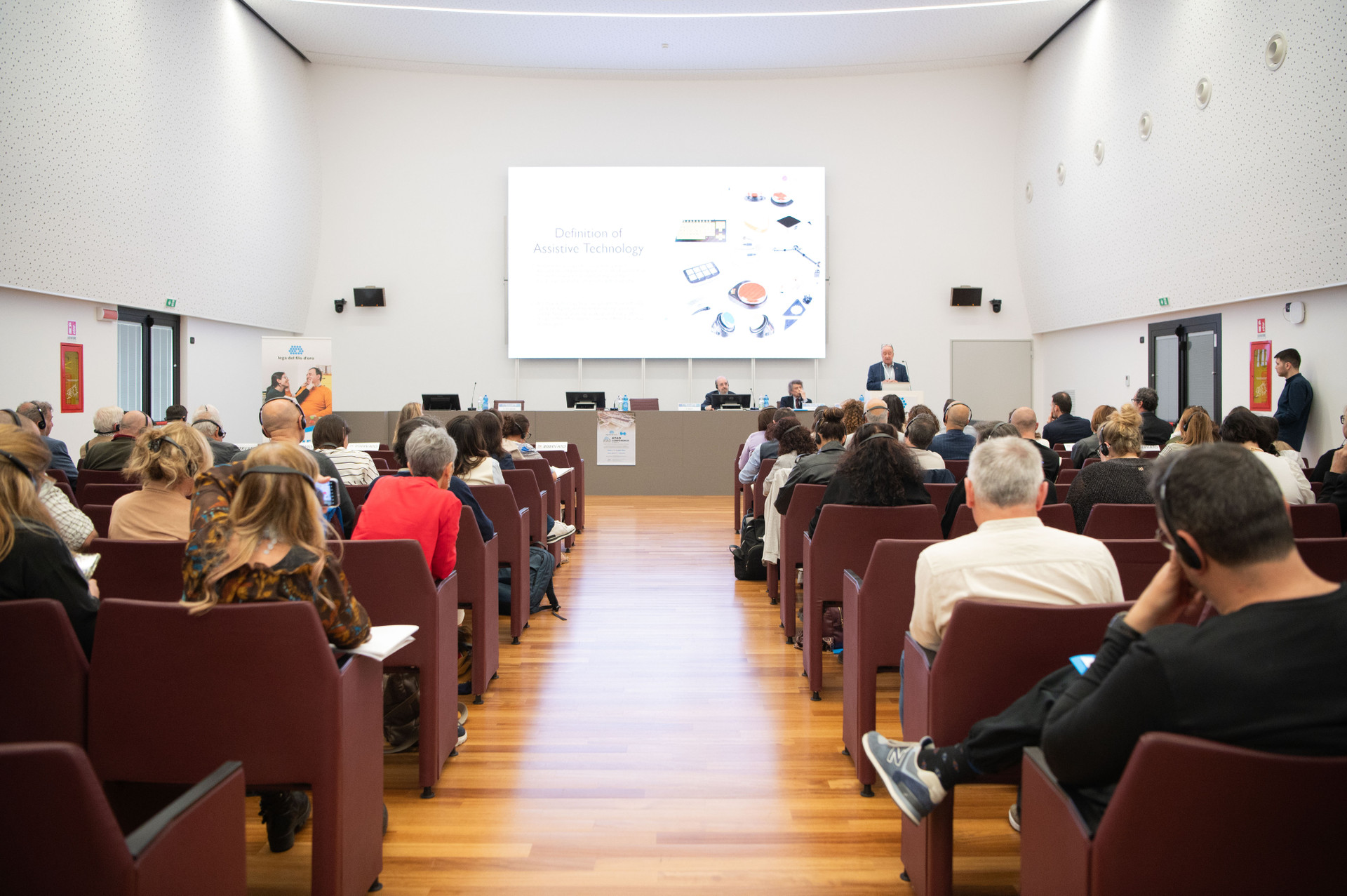 Terza Edizione della Conferenza Internazionale su Tecnologie Assistive e Disabilità. Auditorium della Lega del Filo d'Oro di Osimo gremito di persone sedute sulle poltrone che ascoltano la conferenza.