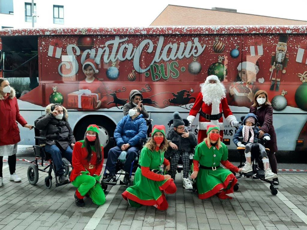 Il bus di Santa Claus in visita al Centro Nazionale della Lega del Filo d'Oro. ALcuni utenti posano assieme a Babbo Natale e a 3 elfe