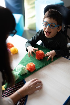 Nicola, bambino con disabilità, fa un lavoretto natalizio con la sua operatrice attaccando dei ponpon su un albero di Natale di feltro.