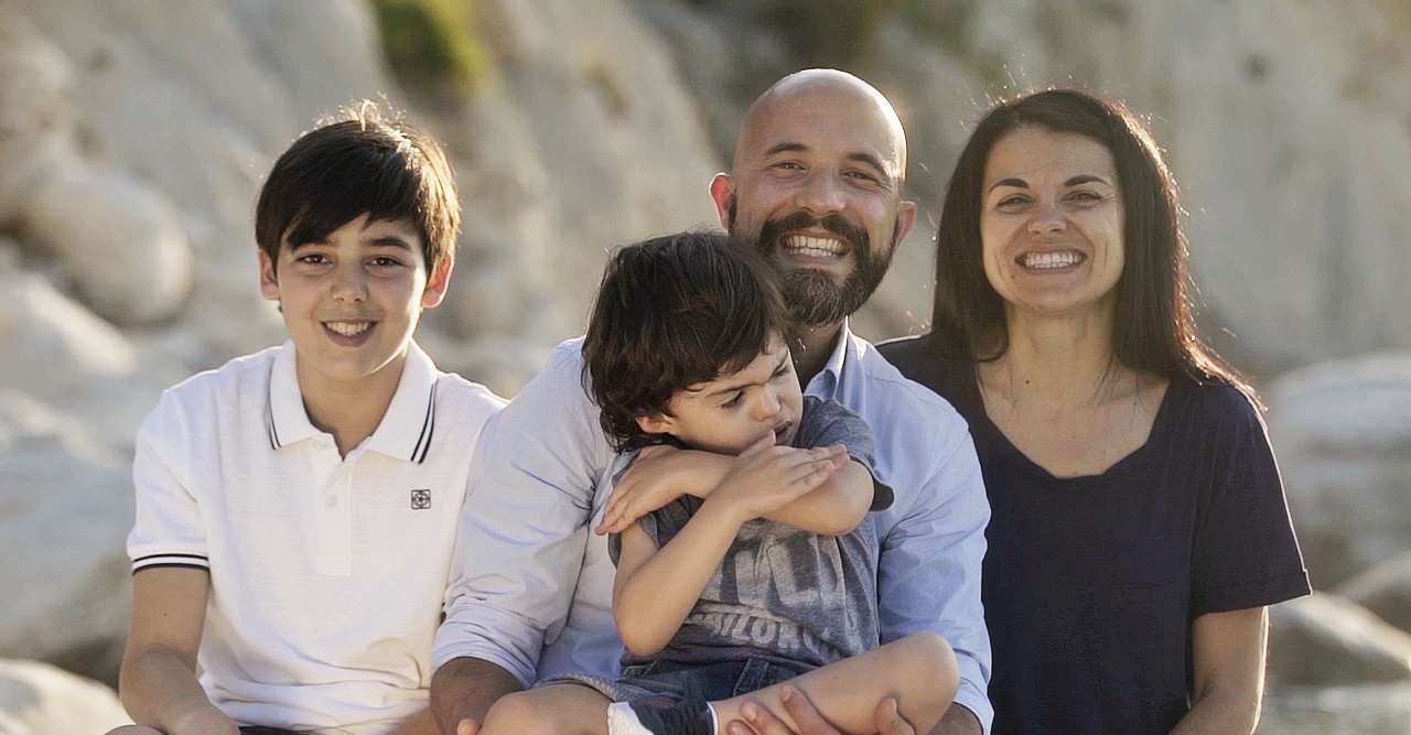 Foto della famiglia di Agostino, bambino con sindrome di Charge seguito a Osimo dalla Lega del Filo d'Oro. Il papà lo tiene in braccio mentre il fratello maggiore e la mamma sorridono al suo fianco