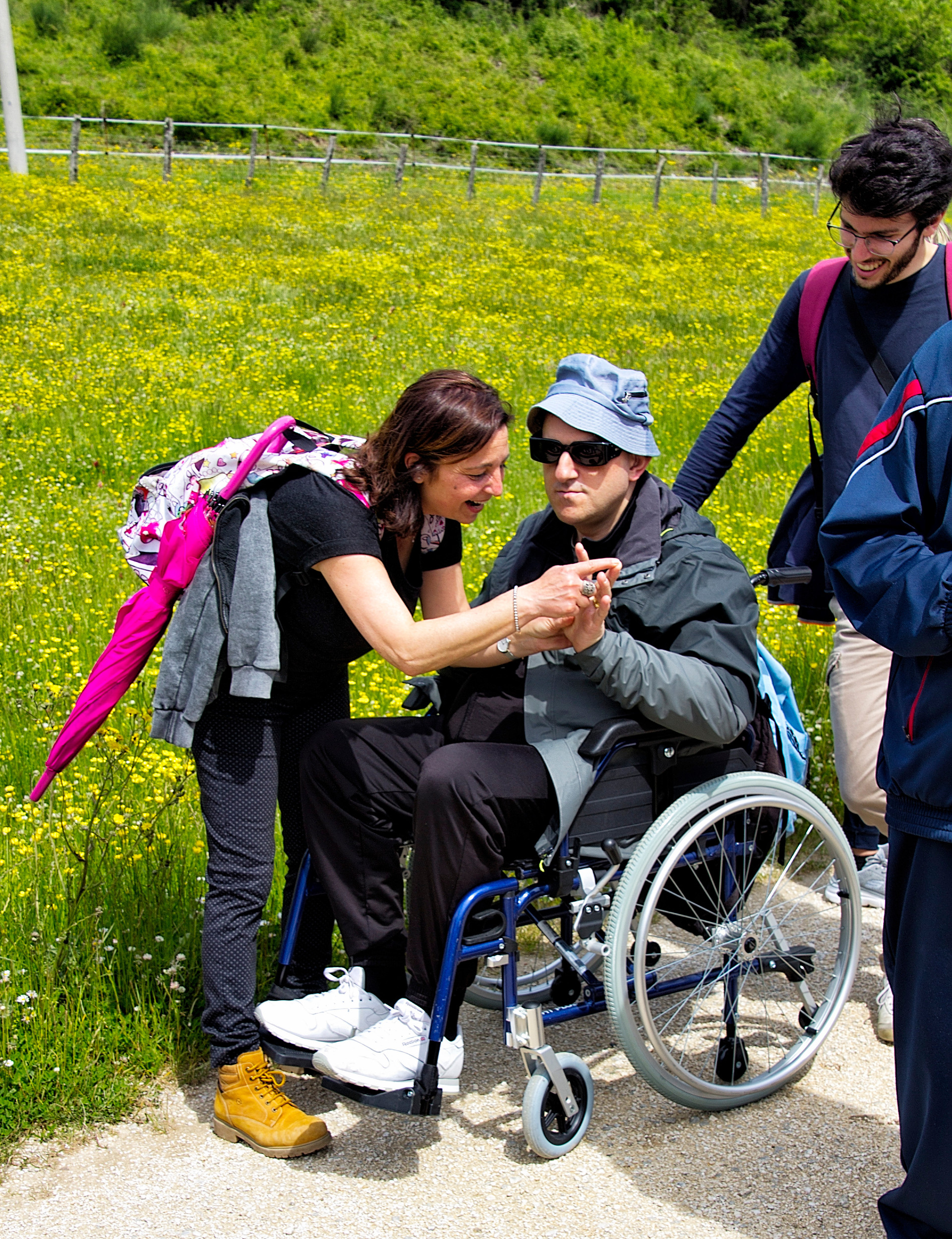 Su un sentiero sterrato un'educatrice comunica in Malossi con un uomo sordocieco con disabilità motoria