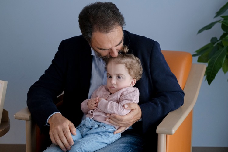 Neri Marcorè è seduto su una poltrona e tiene sopra le sue gambe Benedetta