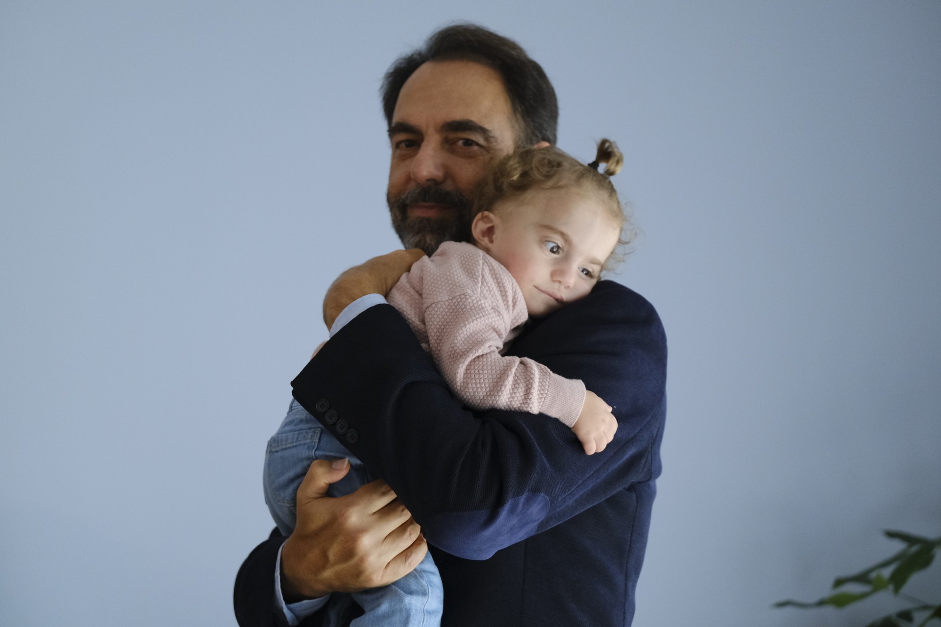 Neri Marcorè tiene in braccio Benedetta, una bambina seguita dalla Lega del Filo d’Oro. La bambina appoggia la testa sulla sua spalla.