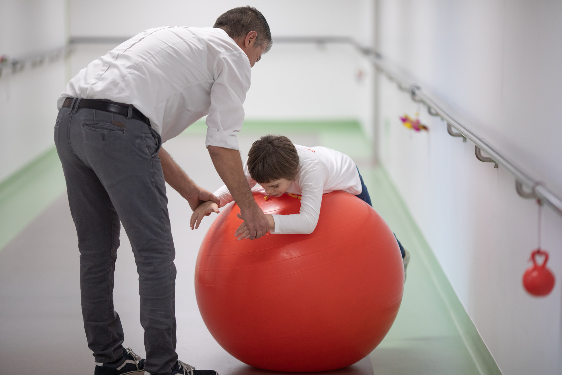 Una bambina a trattamento nel Centro Nazionale gioca con il suo papà e una grande palla, nei corridoi del Centro