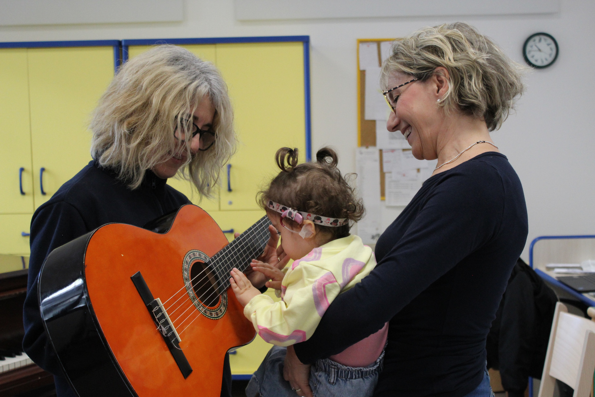 Seduta di musicoterapia. Sophie, una bambina sordocieca di circa 3 anni è in braccio a Manola, l'educatrice. Fiammetta le sta di fronte con la chitarra in mano e pizzica le corde insieme a Sophie