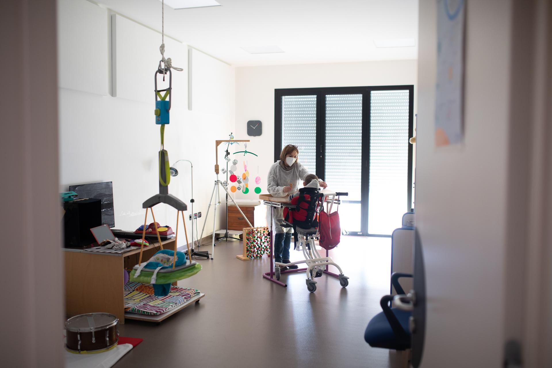 Un'operatrice è in piedi davanti ad un piccolo ospite seduto, per individuare le abilità residue tramite alcuni esercizi di riabilitazione