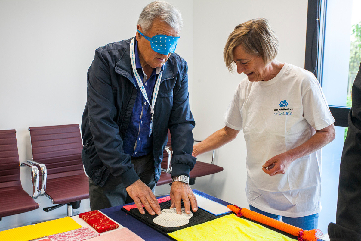 Giornata del Sostenitore - Laboratorio sensoriale - Un sostenitore bendato esplora con le mani dei pannelli con diversi materiali e forme, guidato da una volontaria della "Lega"