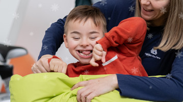 Edoardo, bambino sordocieco, sorride abbracciato alla sua educatrice. Intorno dei fiocchi di neve 