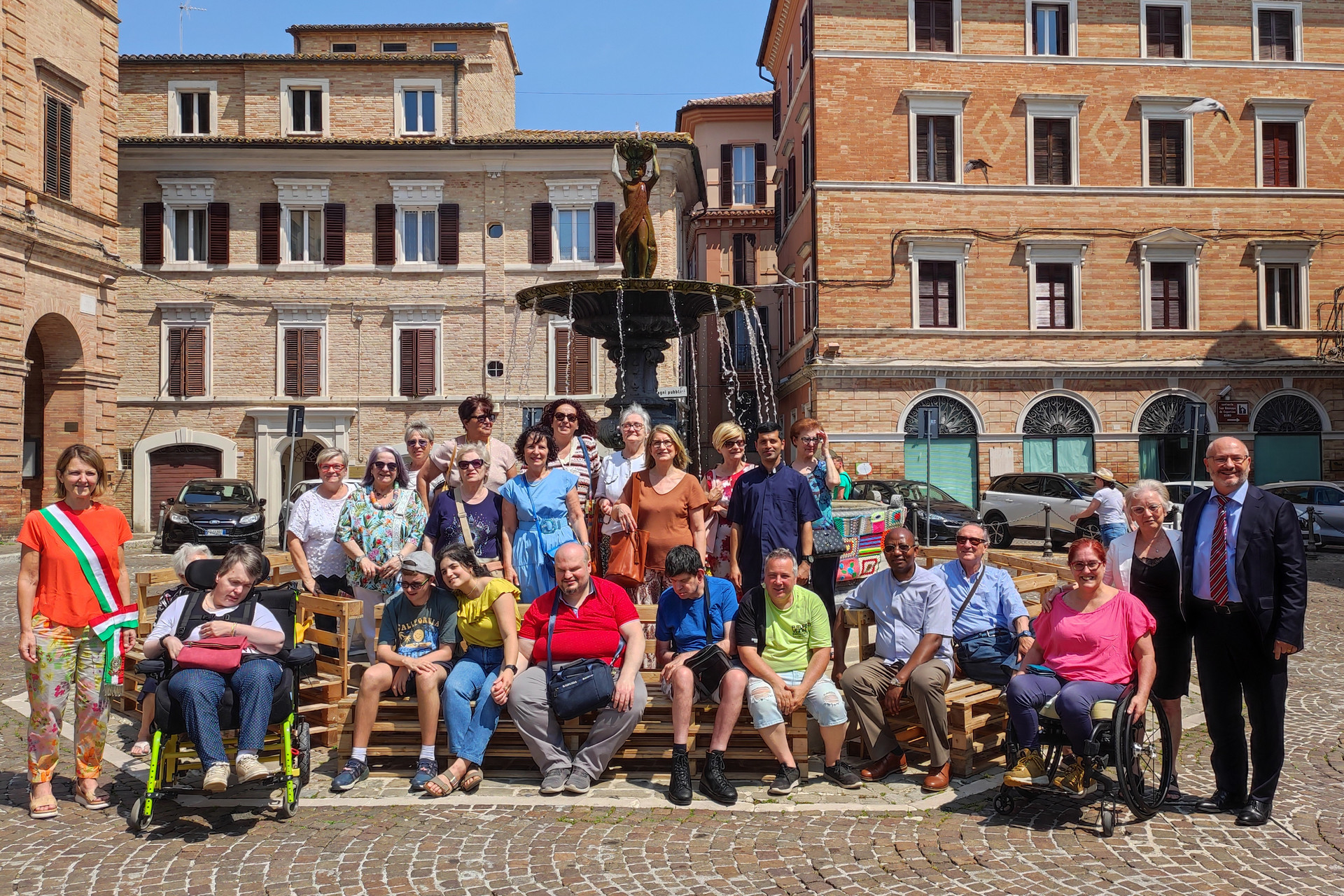 Foto di gruppo scattata in piazza a Osimo davanti alla fontana, durante l’evento di yarn bombing.