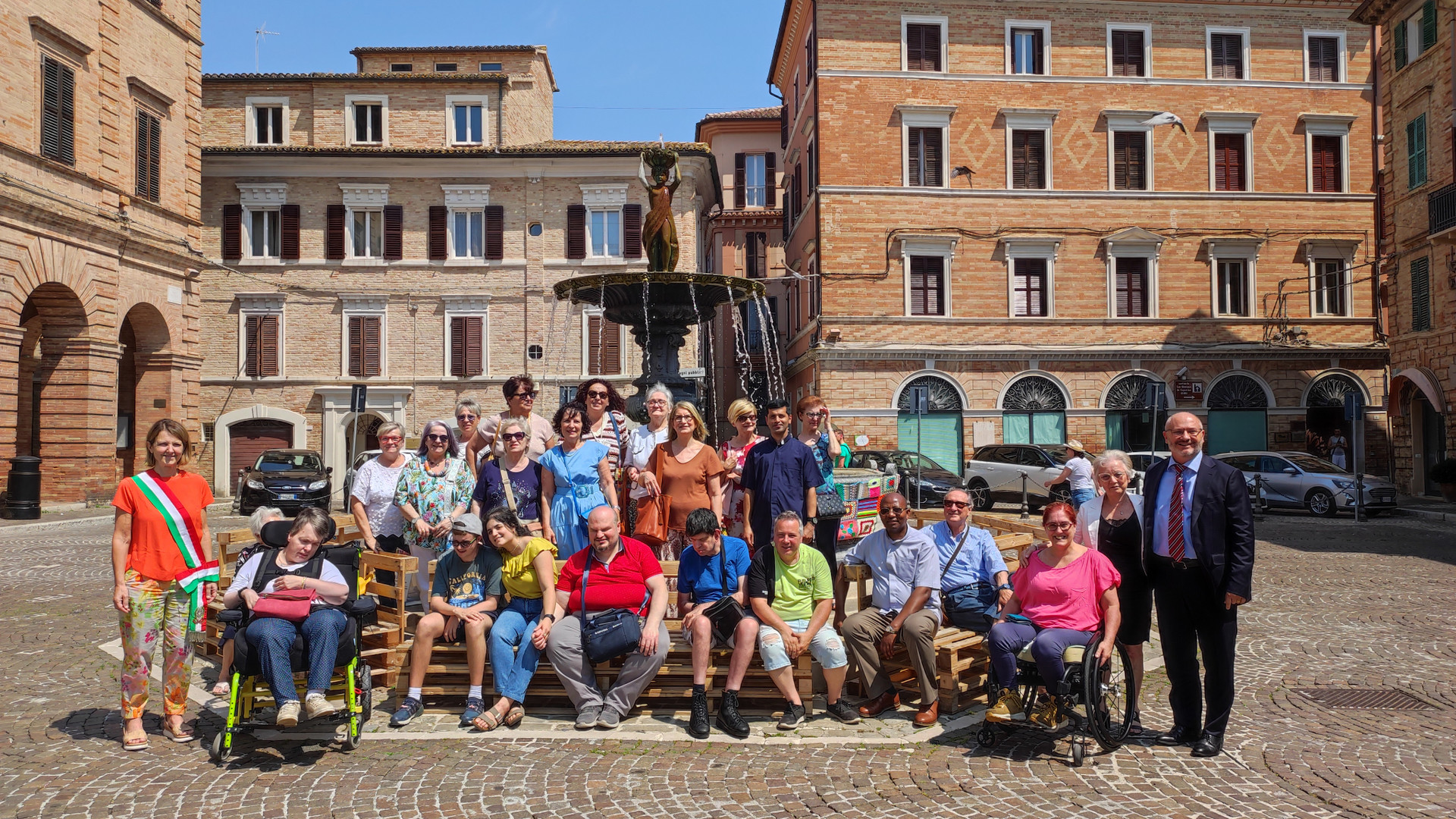 Foto di gruppo scattata in piazza a Osimo davanti alla fontana, durante l’evento di yarn bombing.