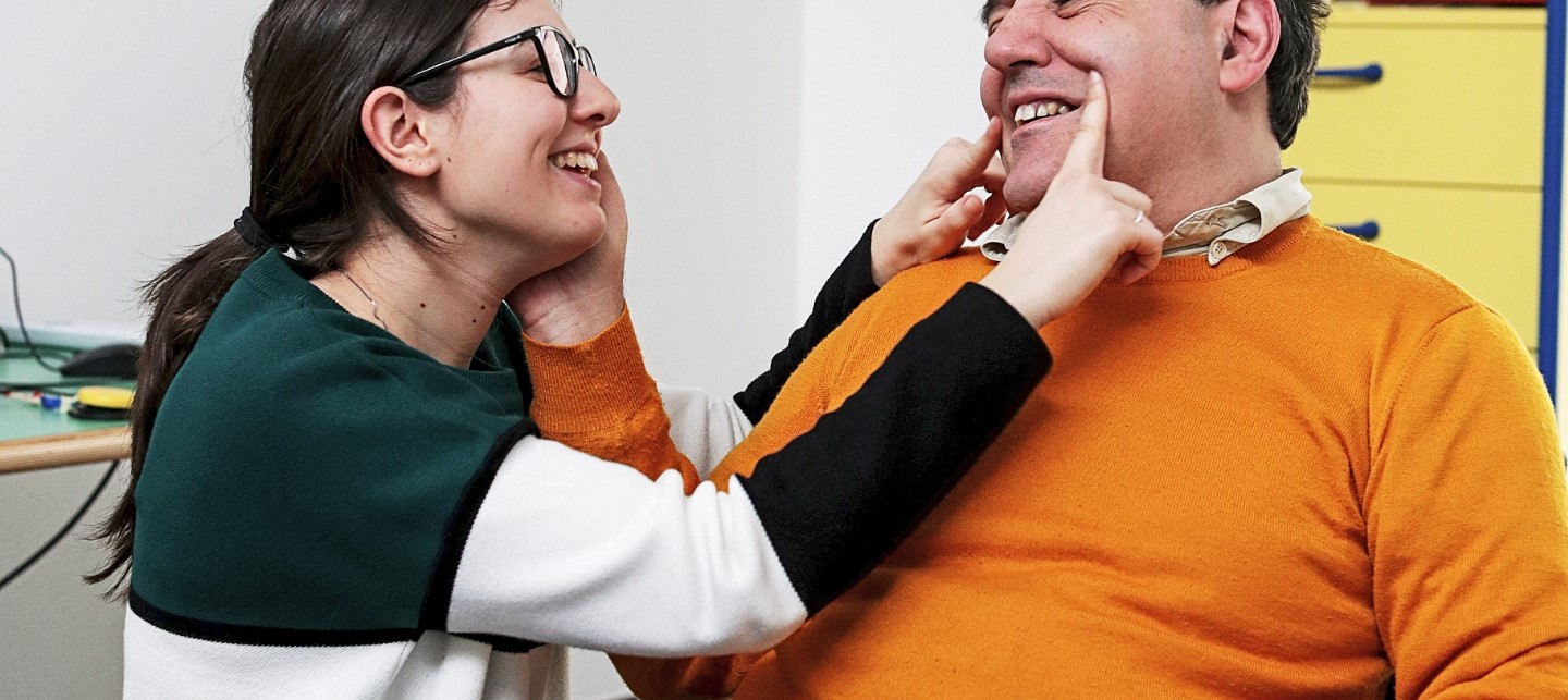 Alberto, utente adulto del Centro di Osimo, posa la mano sul viso di una operatrice, che sorridendo disegna con le dita un sorriso anche sul viso di lui