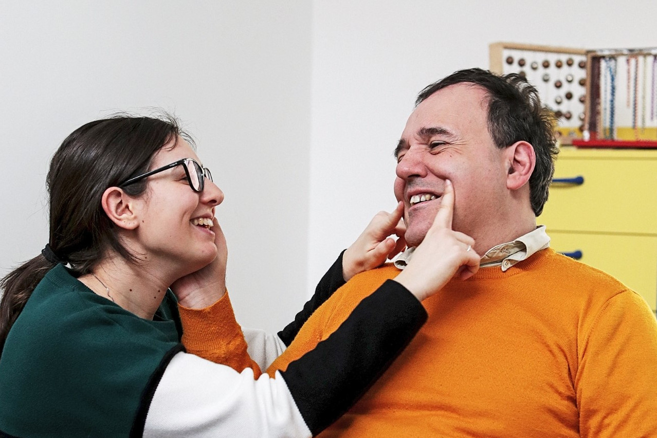 Alberto, utente adulto del Centro di Osimo, posa la mano sul viso di una operatrice, che sorridendo disegna con le dita un sorriso anche sul viso di lui