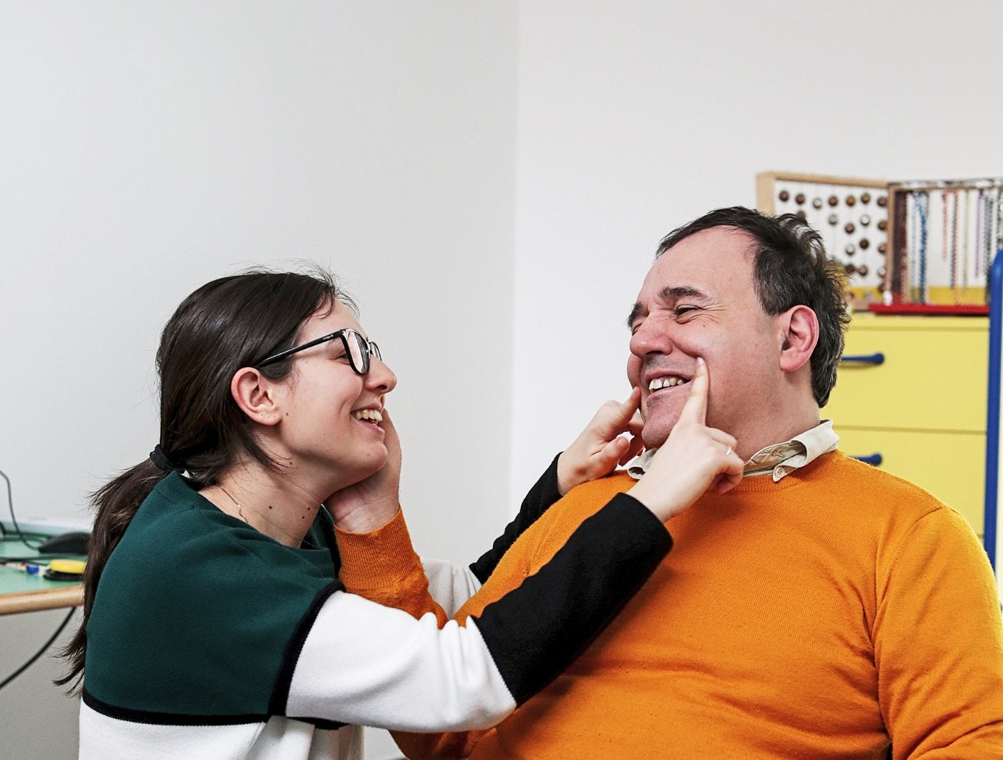 Alberto, utente adulto del Centro di Osimo, posa la mano sul viso di una operatrice, che sorridendo disegna con le dita un sorriso anche sul viso di lui