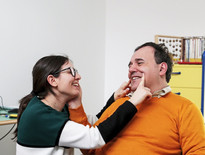 Alberto, utente adulto del Centro di Osimo, posa la mano sul viso di una operatrice, che sorridendo disegna con le dita un sorriso anche sul viso di lui