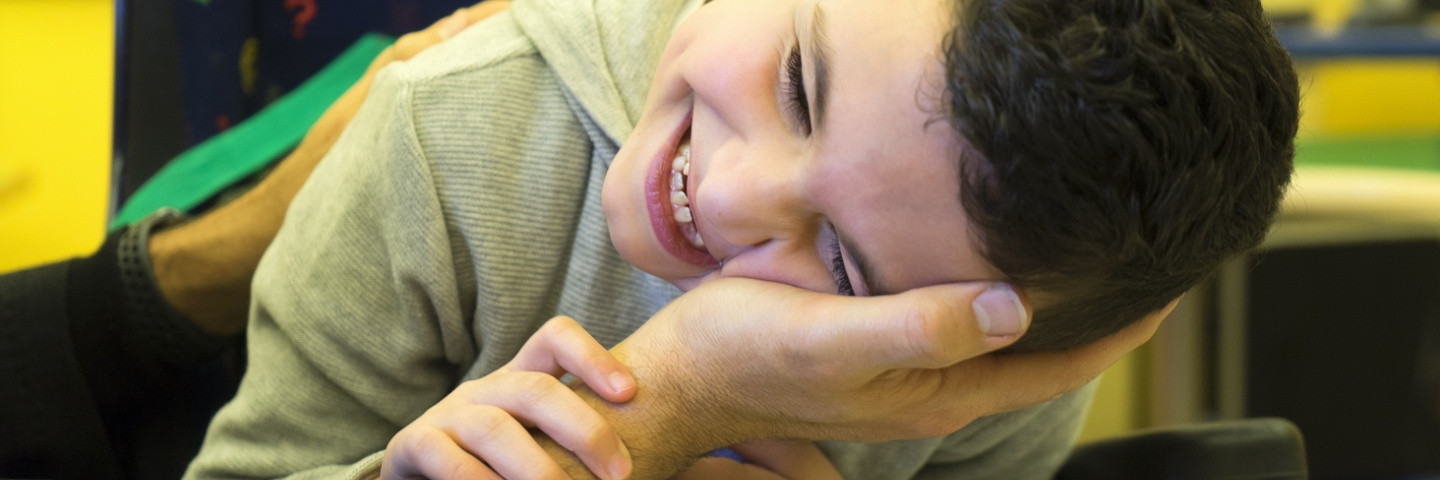 Bambino che porge la testa sulla mano di una persona adulta, che sorride