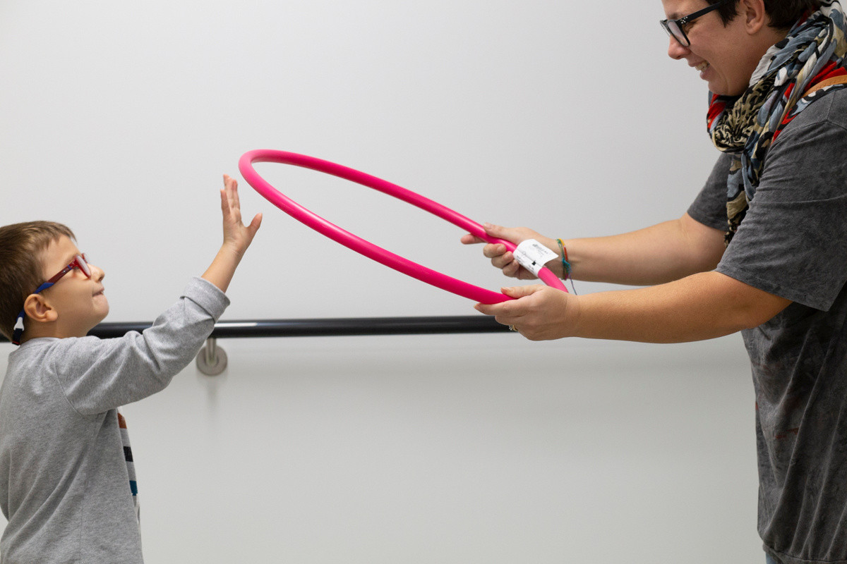 Biagio, piccolo utente del Centro di Osimo, alza una mano per prendere un hulahop rosa che la sua educatrice gli sta porgendo