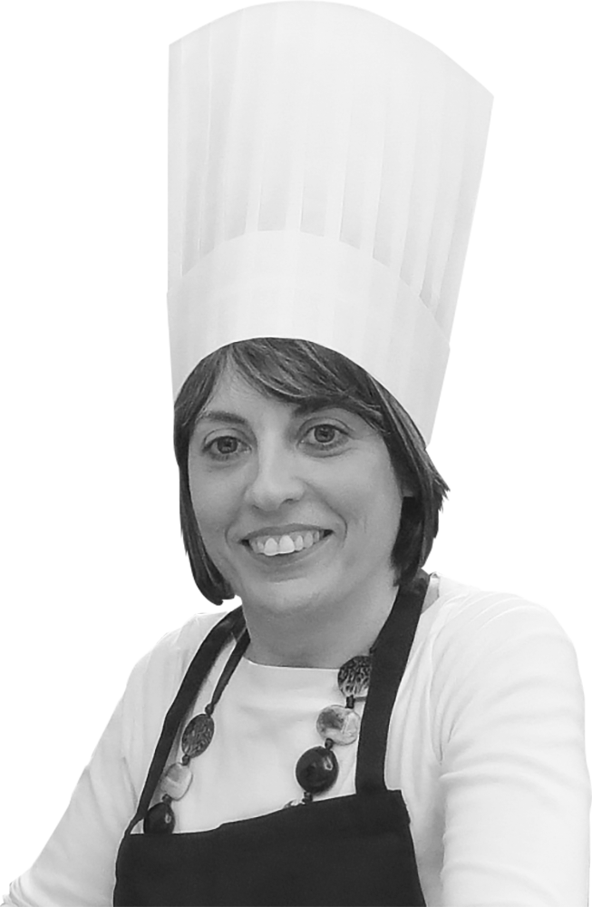 Simona, utente seguita dalla Lega del Filo d'Oro, è ritratta con un grande cappello bianco da cuoco su uno sfondo completamente nero.