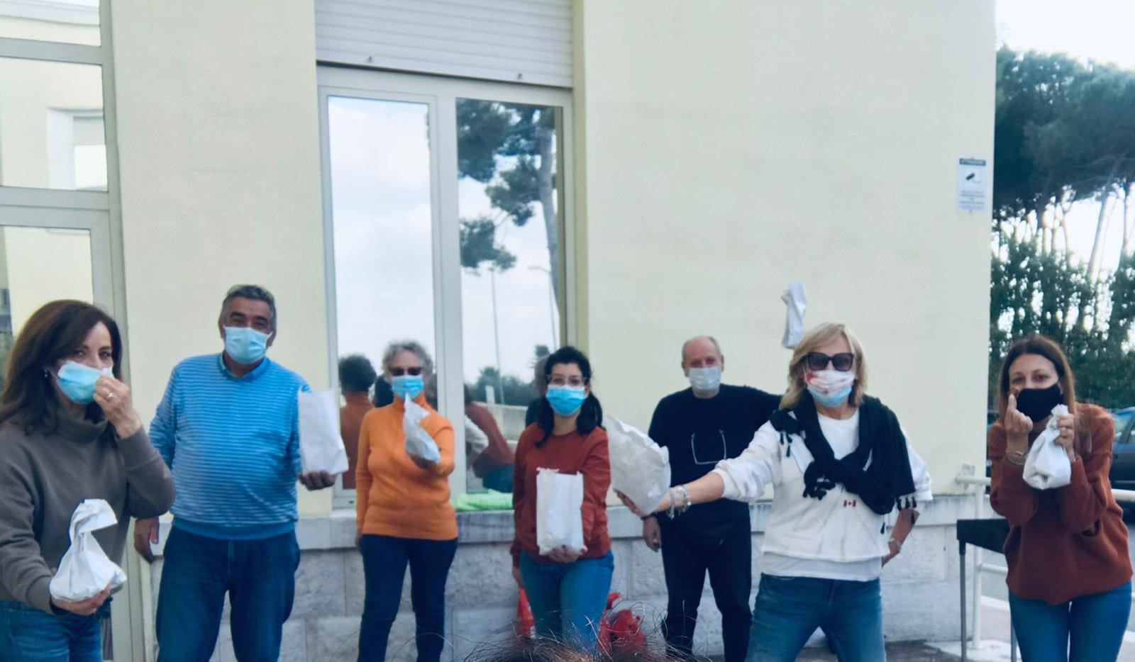 Un gruppo di volontari con mascherina mostra i sacchetti con le caldarroste appena preparati.