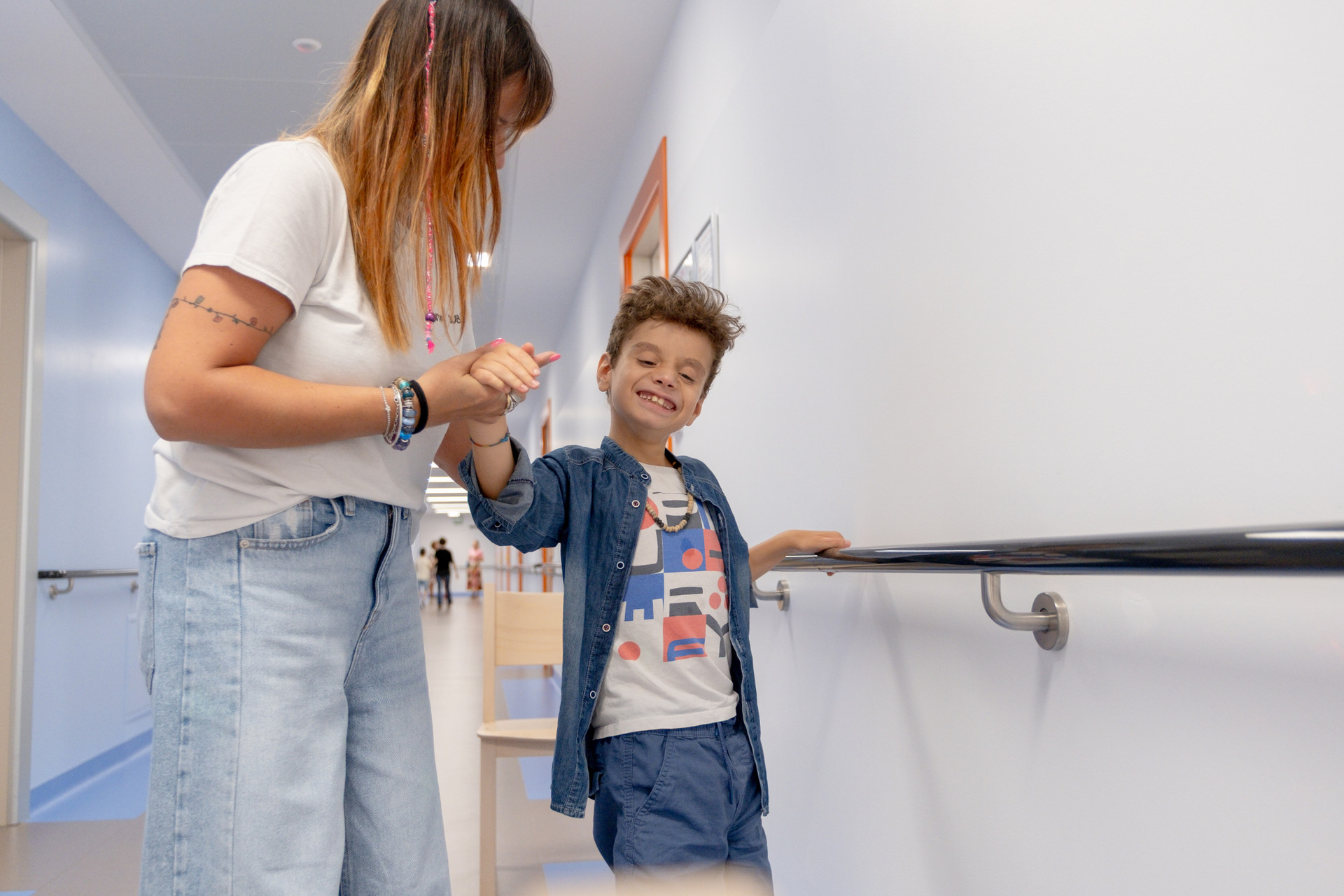 Antonio, bambino a trattamento presso il Centro Nazionale di Osimo, cammina per mano con la sua educatrice reggendosi a un corrimano presente nel corridoio del Centro