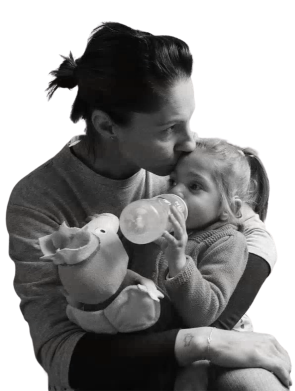 Foto in bianco e nero di Sveva che beve dal biberon in braccio alla mamma, che le dà un bacio sulla fronte