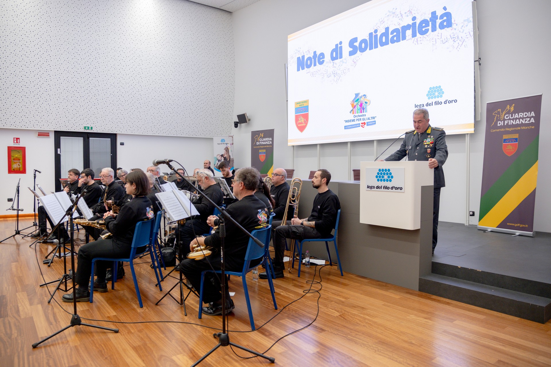 Nello scatto compaino i musicisti che si sono esibiti durante il Concerto dell’Orchestra Insieme per gli Altri che ha visto la partecipazione della Guardia di Finanza regionale delle Marche. Nello scatto compare anche il Comandante Regionale della Guardia di Finanza, Altiero, mentre tiene un discorso.
