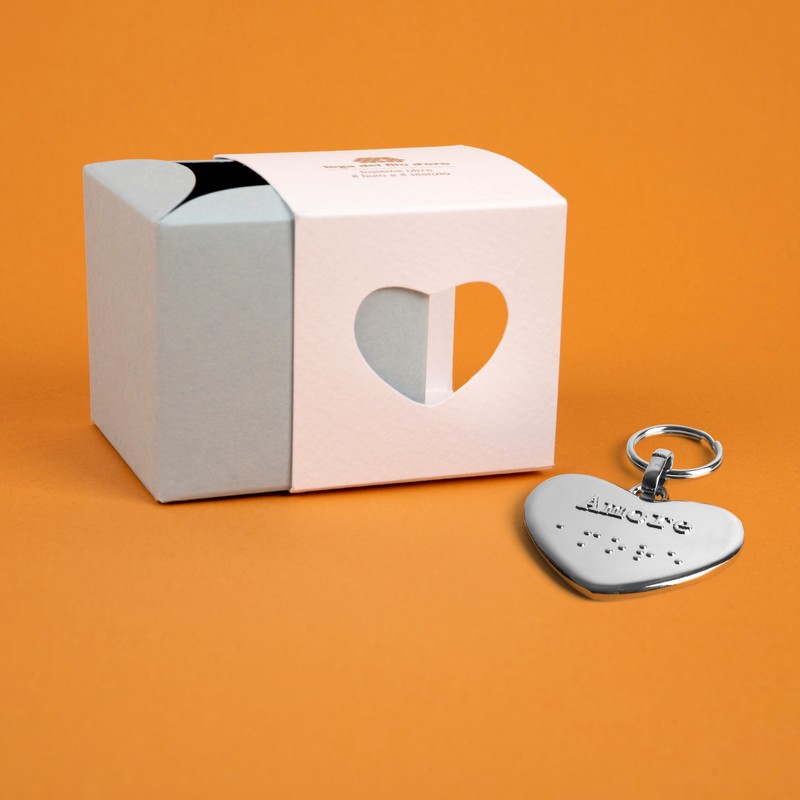 Bomboniera composta da due scatoline in cartoncino pregiato inserite l'una nell'altra. Quella esterna è bianca, quella interna, visibile da un'apertura a forma di cuore, è celeste. Accompagnata dal suo portachiavi cuore