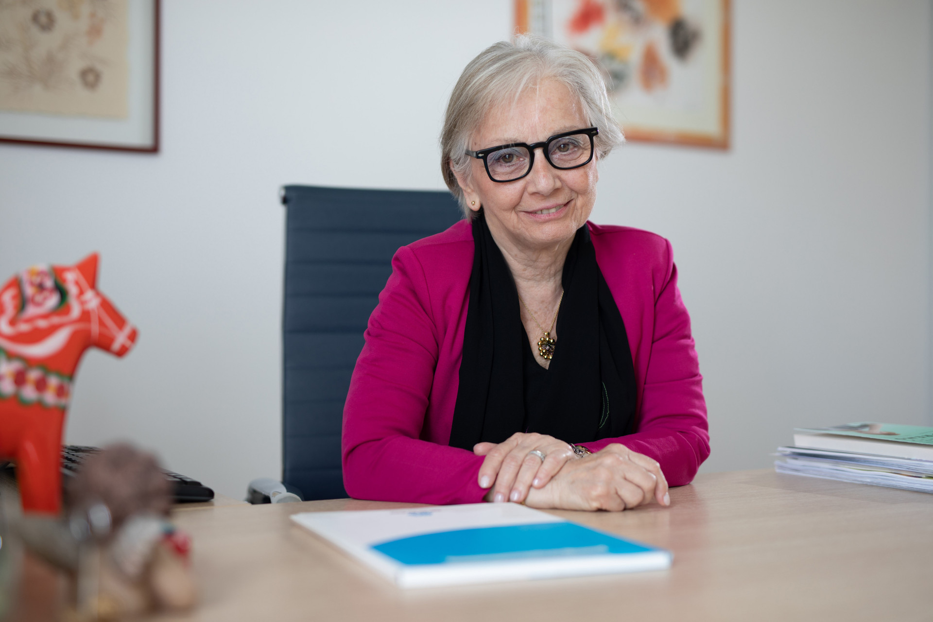 Patrizia Ceccarani, Segretario del Comitato Tecnico Scientifico ed Etico della Lega del Filo d'Oro, seduta nel suo ufficio sorride di fronte alla fotocamera. Indossa un vestito nero con una giacca fucsia.