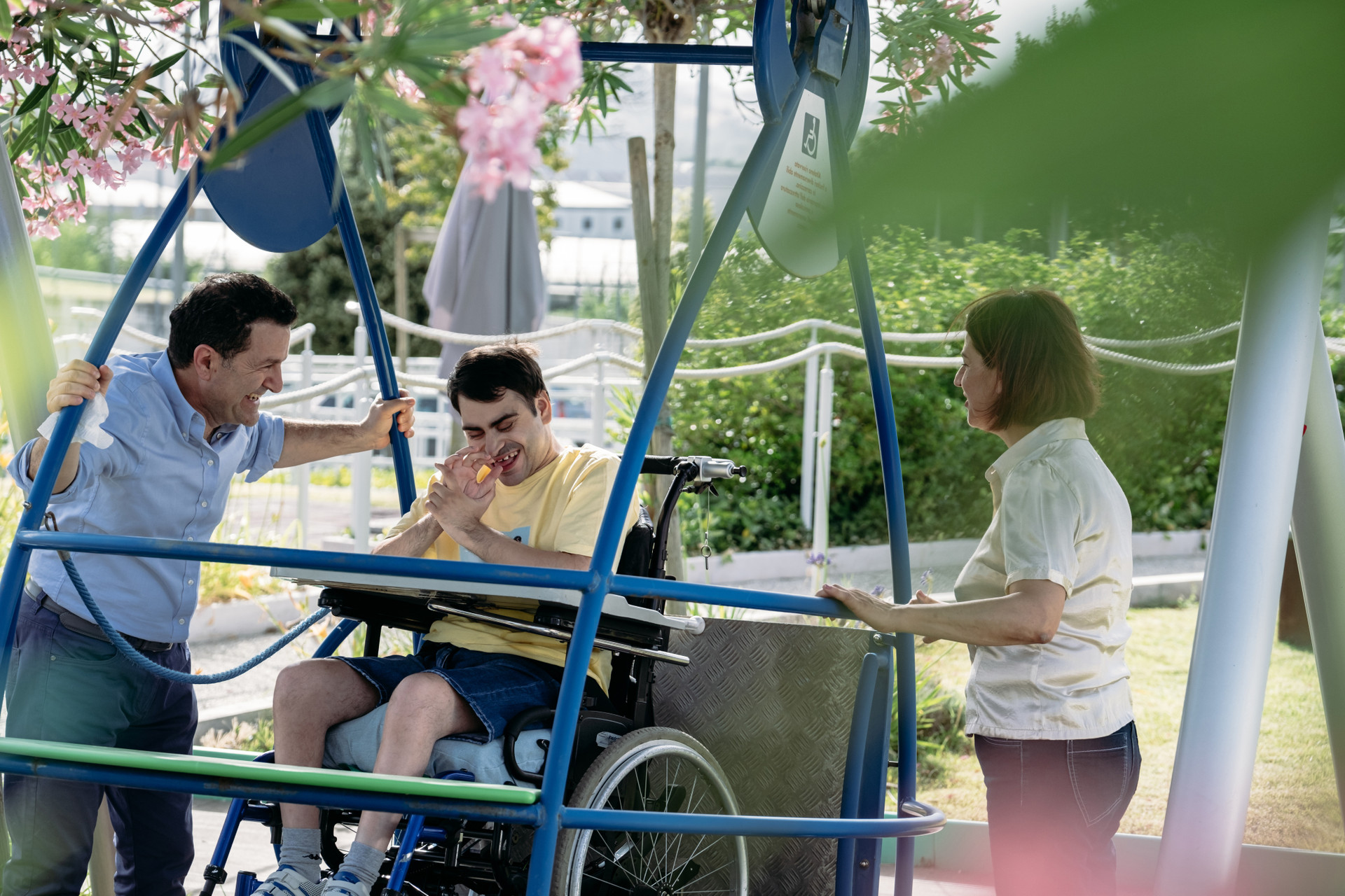 Simone, un utente aulto della Lega del Filo d'Oro in un altalena con i suoi genitori in una giornatanta di sole