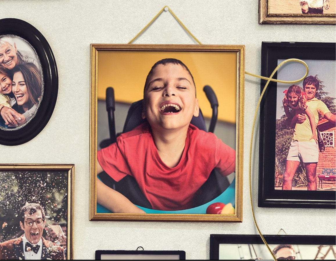 Ci sono alcuni quadri appesi a una parete, con immagini della vita di una famiglia. Al centro spicca il quadro, appeso tramite un filo d'oro, raffigurante Francesco, un bambino utente della Lega del Filo d'Oro, sorridente.