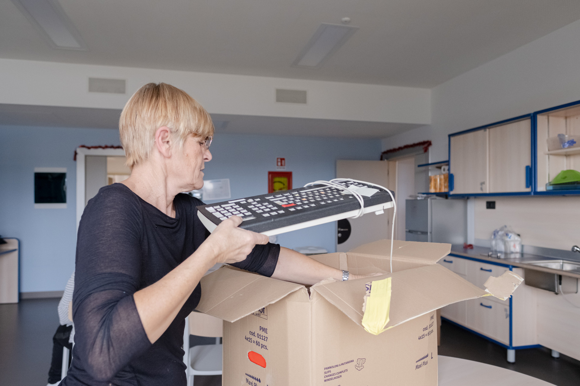 Operatrice inizia a disfare gli scatoloni per prendere gli ausili personalizzati per i nuovi ospiti residenziali del Centro Nazionale di Osimo, come una tastiera
