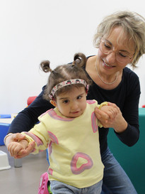Sophie, bambina sordocieca con la sindrome di Charge, insieme alla sua educatrice.- L'educatrice è in ginocchio e sta aiutando Sophie a camminare