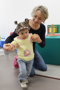 Sophie, bambina sordocieca con la sindrome di Charge, insieme alla sua educatrice.- L'educatrice è in ginocchio e sta aiutando Sophie a camminare