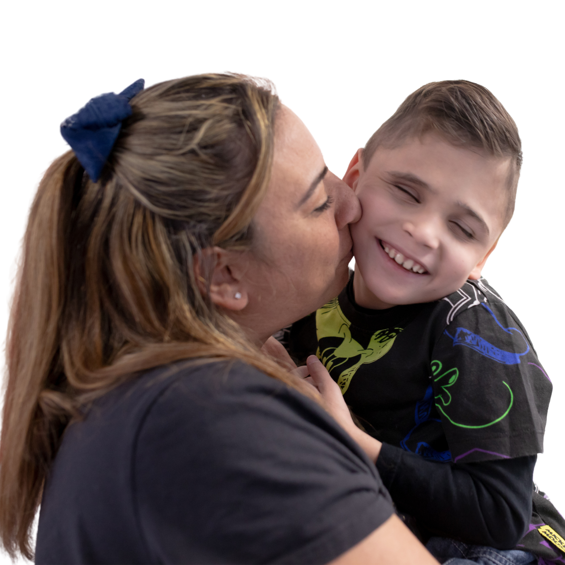 Foto in primo piano di Matteo, un bambino sordocieco e della sua mamma. La mamma lo abbraccia e gli dà un bacio sulla guancia. Matteo è felice, sorride. Lo sfondo è neutro