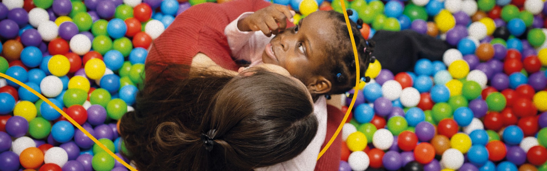 Bambina gioca in una vasca di palline colorate insieme a un’operatrice. Immagine che esprime relazione, gioco e stimolazione sensoriale in un contesto educativo inclusivo.
