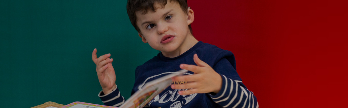Agostino, un bambino utente della Lega del Filo d'Oro, è intento a sfogliare un libro tattile. L'immagine cattura un momento di concentrazione e scoperta, evidenziando l'importanza dell'accessibilità e dell'inclusione.