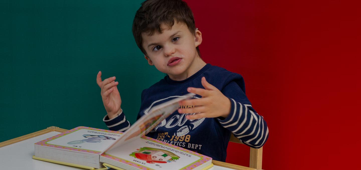 Agostino, un bambino utente della Lega del Filo d'Oro, è intento a sfogliare un libro tattile. L'immagine cattura un momento di concentrazione e scoperta, evidenziando l'importanza dell'accessibilità e dell'inclusione.