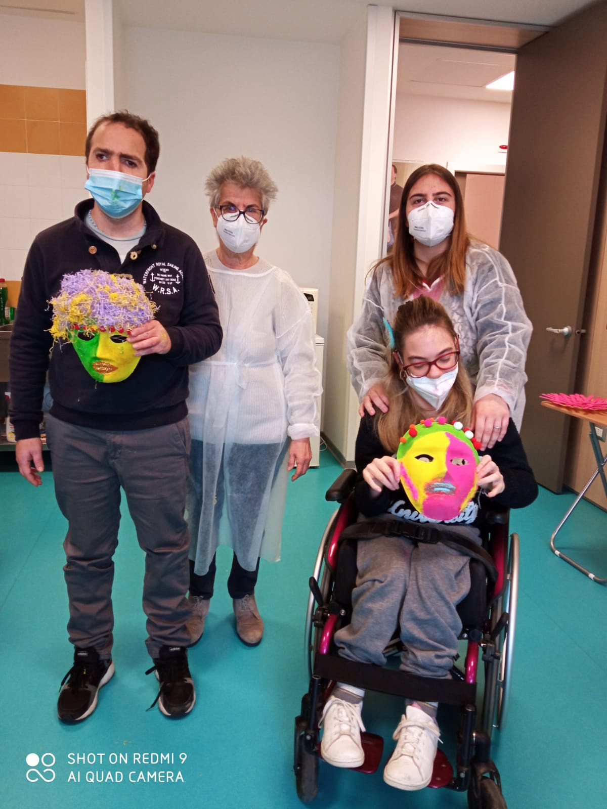 Due utenti mostrano le maschere realizzate durante un laboratorio per carnevale. Dietro di loro ci sono due volontarie che hanno partecipato al laboratorio.