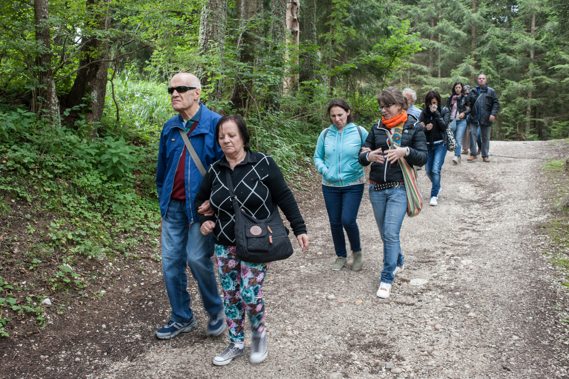 Uscite nella natura. Un gruppo di utenti passeggia su un sentiero di montagna, ciascuno accompagnato a braccetto da un volontario della Lega del Filo d'Oro