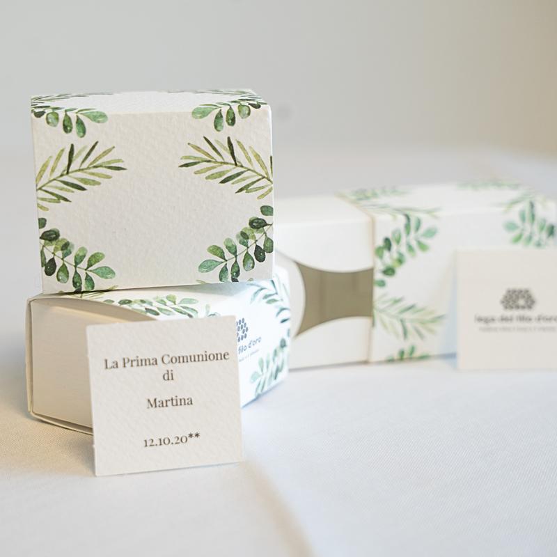 3 bomboniere in cartoncino bianco, decorate da un motivo verde a foglie. Accompagnate da un bigliettino personalizzato di esempio, con scritto "La prima Comunione di Martina" e la data