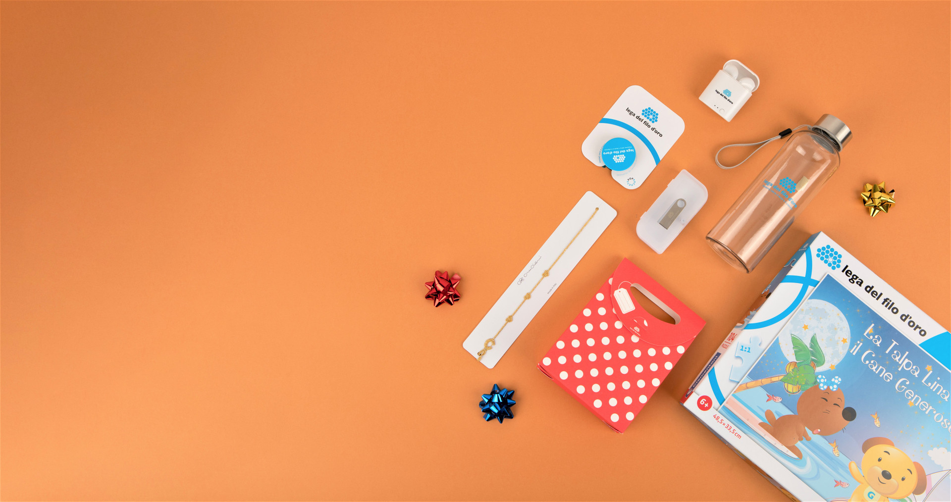 Composizione di regali solidali su sfondo arancione, inclusi auricolari, pop grip, chiavetta USB, borraccia in tritan e braccialetto Cruciani. Perfetti per donare con stile e solidarietà.