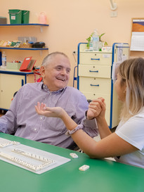 Fabio, utente adulto del Centro di Osimo, gioca una partita di domino con una volontaria, i due si tengono la mano e sorridono divertiti