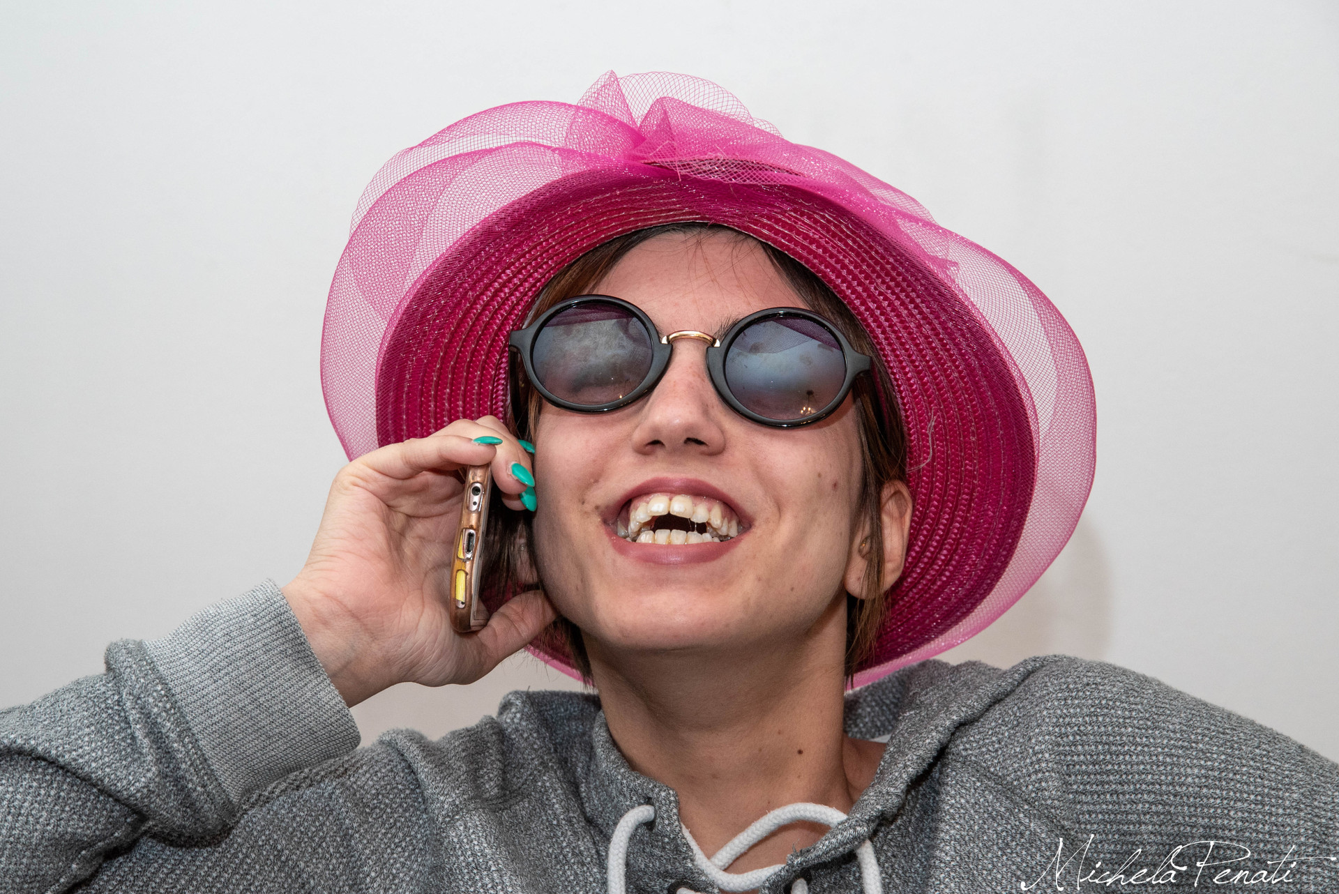 Francesca, giovane utente sordocieca seguita dal Centro di Lesmo, parla al telefono con un grande sorriso. Indossa occhiali da sole e un cappello fucsia.