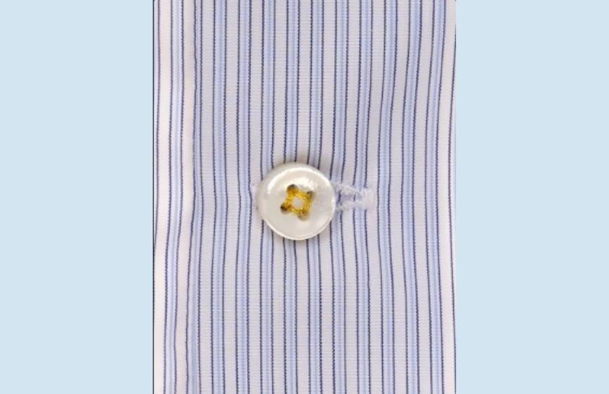 Primo piano di un bottone bianco cucito con filo giallo su una camicia a righe sottili verticali blu e bianche.