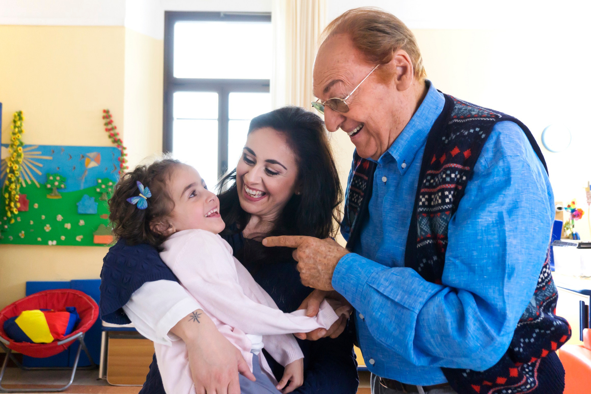 Foto di gruppo sorridente di Renzo Arbore con Sofia, bimba seguita dalla Lega del Filo d'Oro, e la sua mamma