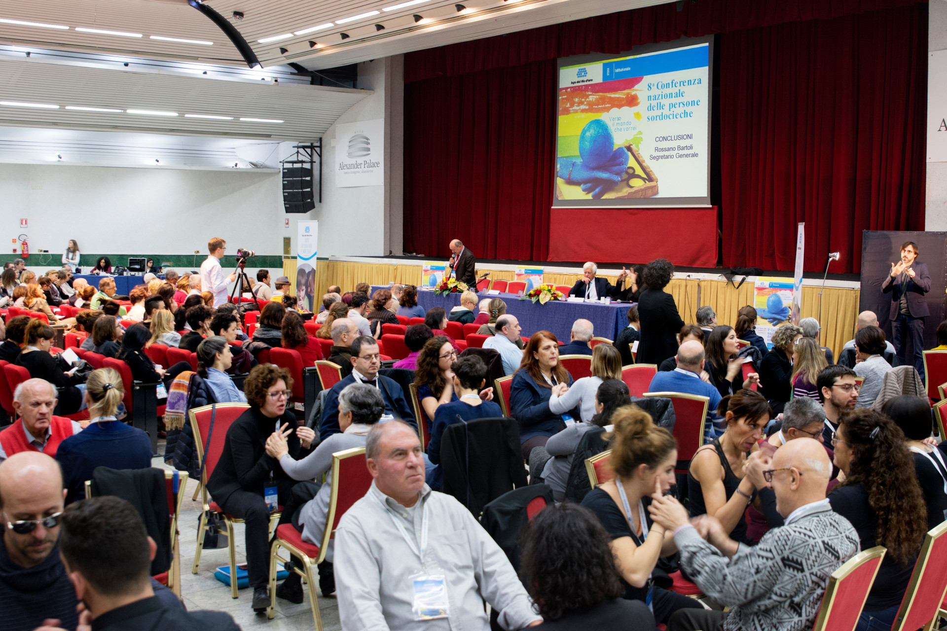 Conferenza nazionale delle persone sordocieche anno 2018. vista della platea. tante persone sordocieche e interpreti comunicano tra loro in LIS, LIS tattile e Malossi