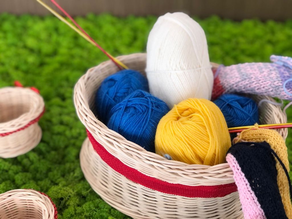 Alcuni gomitoli colorati e i ferri per lavorare a maglia sono contenuti in un cestino. 