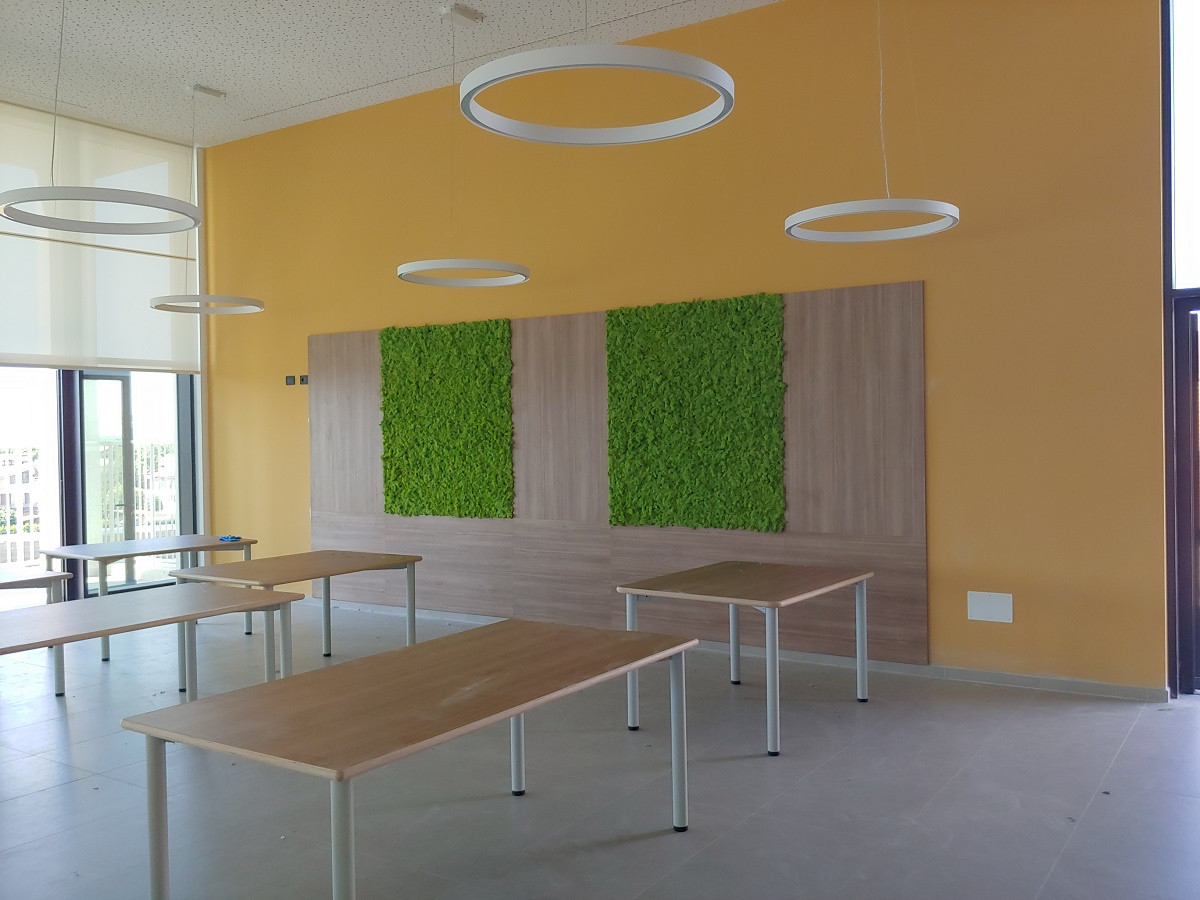 Interno della mensa del Centro Nazionale di Osimo, tavoli e lampadari, con parete di fondo arancione e muschio stabilizzato.